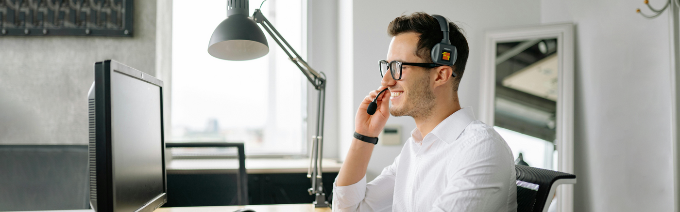 Man in a white shirt using a computer and headset in an office setting